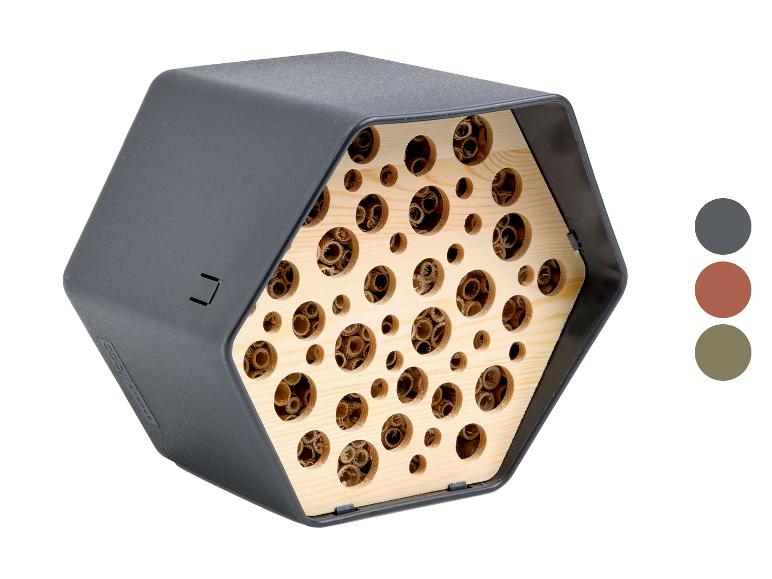 Hôtel à insectes hexagonal avec intérieur en bois et trous de différentes tailles, en gris foncé.