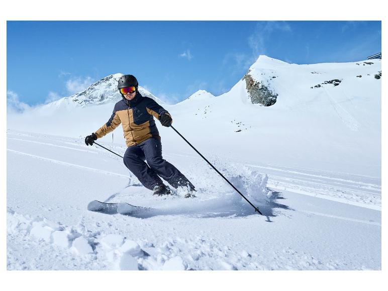 Un homme en veste et pantalon de ski descend à ski une pente en montagne.