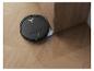 Robot aspirateur noir nettoyant un parquet à côté d'un meuble en bois.