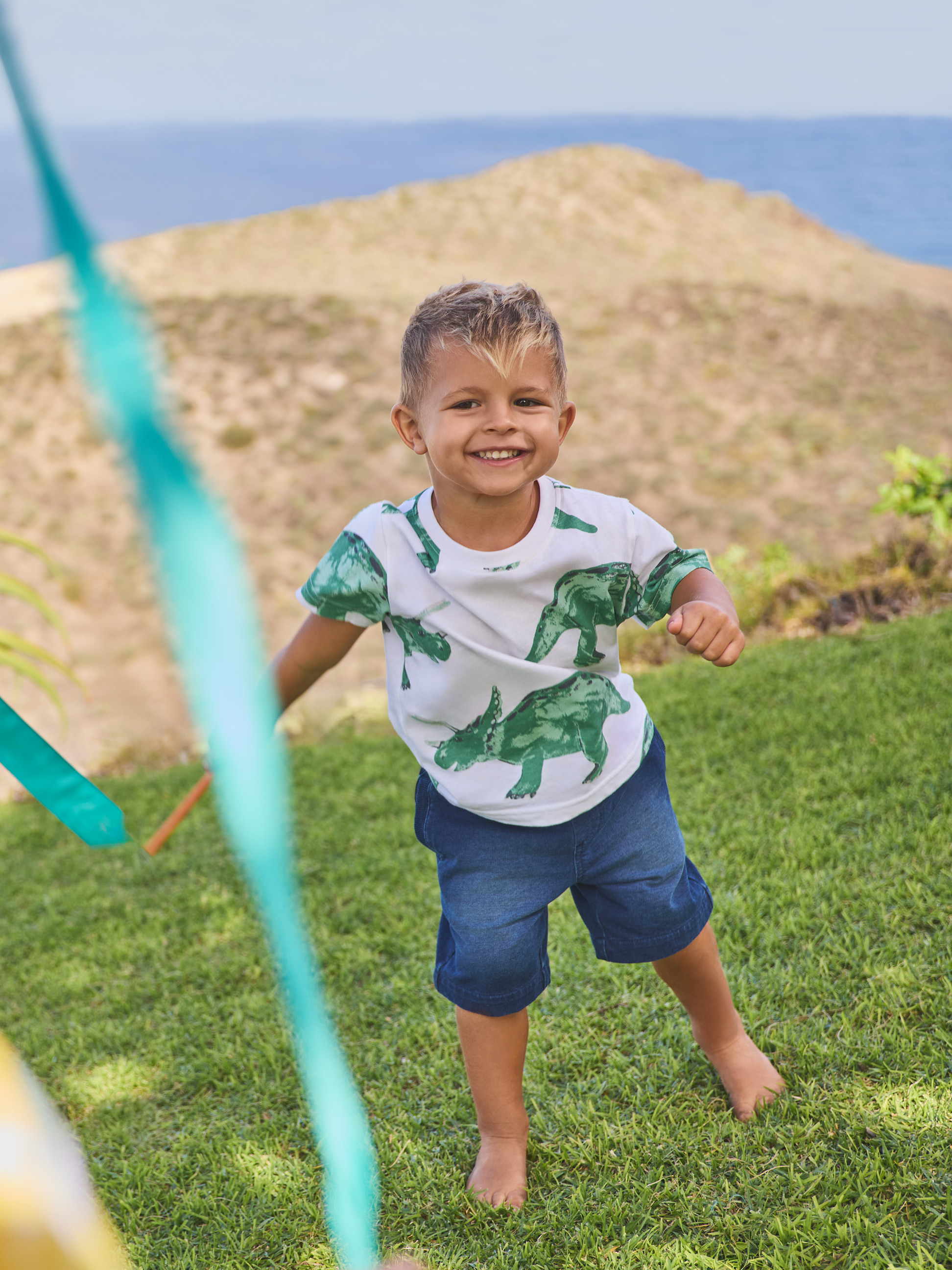 Garçon en t-shirt dinosaure et short en jean, jouant à l'extérieur.