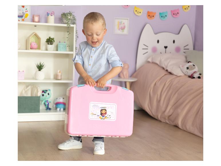 Un garçon tient une mallette de jouets rose Gabby's Dollhouse dans une chambre d'enfant.