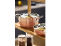 Casseroles et poêles en cuivre sur une étagère en bois dans la cuisine.