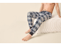 Homme torse nu en pyjama à carreaux bleu et blanc, assis sur un pouf blanc.