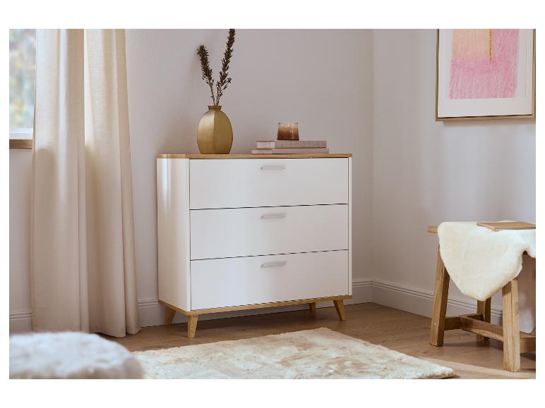 Commode blanche à trois tiroirs, décorée d'un vase doré et d'une bougie, près d'un rideau beige.
