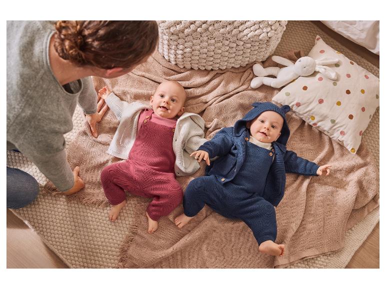 Un adulte et deux bébés en barboteuses tricotées sur une couverture.