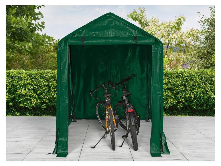 Abri à vélos vert avec deux vélos garés à l'intérieur, sur une terrasse pavée.