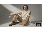 Femme en pull col roulé beige, pantalon marron clair et bottines marrons assise au sol