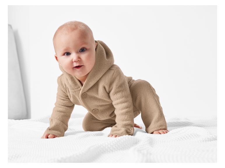 Un bébé rampe sur une couverture blanche avec un pyjama en laine.