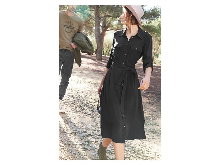 Une femme porte une robe noire avec une ceinture et un chapeau, tandis qu'un homme porte un t-shirt avec un imprimé d'avion.