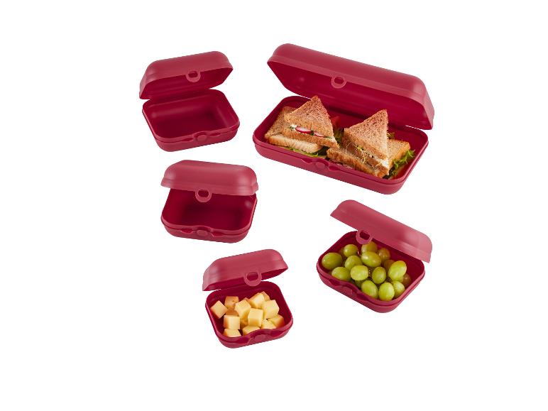 Boîtes repas rouges avec sandwichs et fruits.