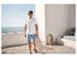 Homme en polo blanc et short en jean sur une terrasse avec vue sur la mer.
