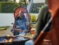 Une femme fait griller des petits pains au-dessus d'un feu de camp, assise dans un fauteuil suspendu.