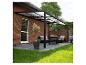 Pergola de terrasse avec cadre noir et toit transparent, mobilier d'extérieur et plantes.