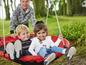 Deux enfants sur une balançoire rouge dans le jardin.