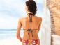 Une femme en bikini noir et short à imprimé floral, regardant l'océan.