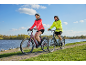Un homme et une femme font du vélo sur un chemin pavé au bord de l'eau.
