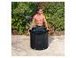 Homme dans une baignoire de glace noire sur une terrasse, entouré de buissons verts.