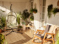 Un balcon avec un fauteuil suspendu, un fauteuil à bascule et des plantes.