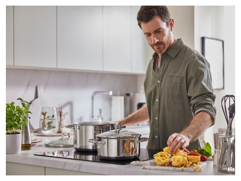 Un homme dans la cuisine, avec deux casseroles sur une plaque à induction et des pâtes fraîches sur une planche à découper.
