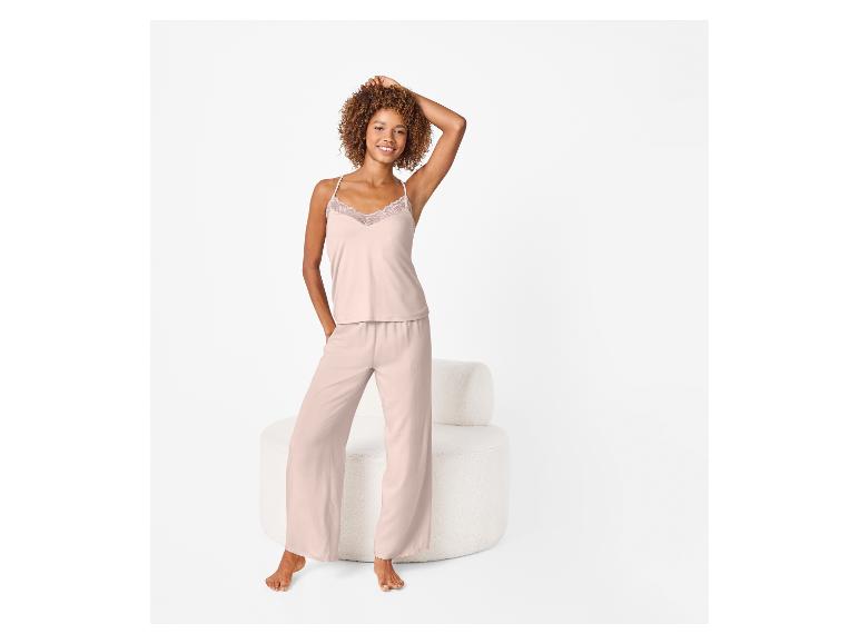 Femme en pyjama rose avec un haut en dentelle, debout à côté d'un fauteuil blanc.