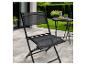 Chaise de jardin pliante noire sur une terrasse avec une table de jardin et une pelouse verte.