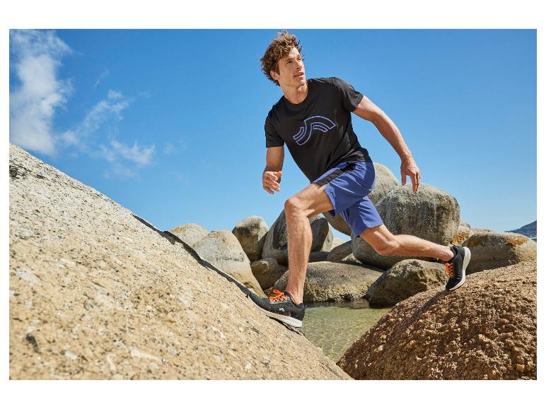 Homme en t-shirt noir et short bleu courant sur des rochers.