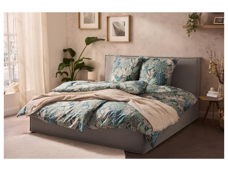 Lit avec parure de lit à motif tropical, couverture beige et plantes dans une chambre lumineuse.