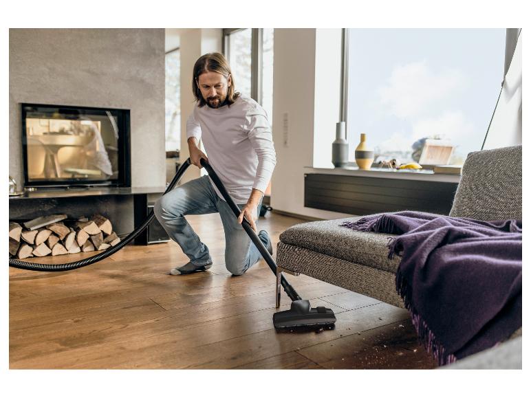 Homme passant l'aspirateur sur un parquet, avec cheminée et canapé en arrière-plan.