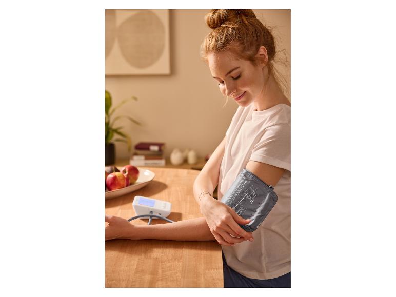 Une femme mesure sa tension artérielle à la maison avec un tensiomètre.
