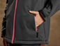 Une veste softshell noire avec une fermeture éclair rose et une poche à fermeture éclair.