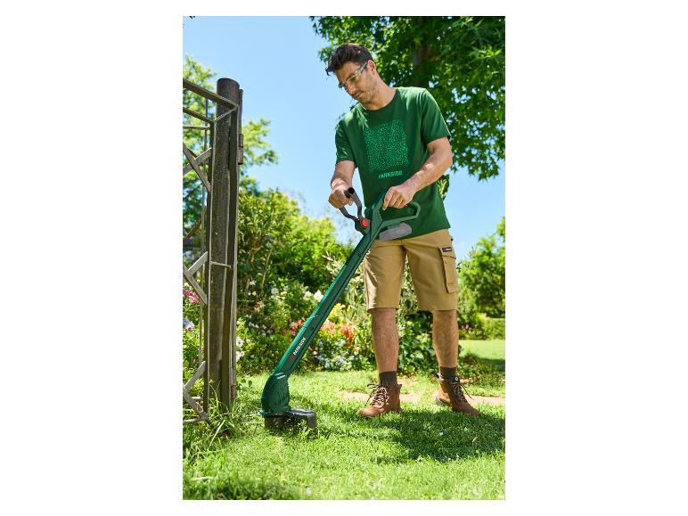 Homme en t-shirt vert et short utilisant un coupe-bordure près d'une clôture.