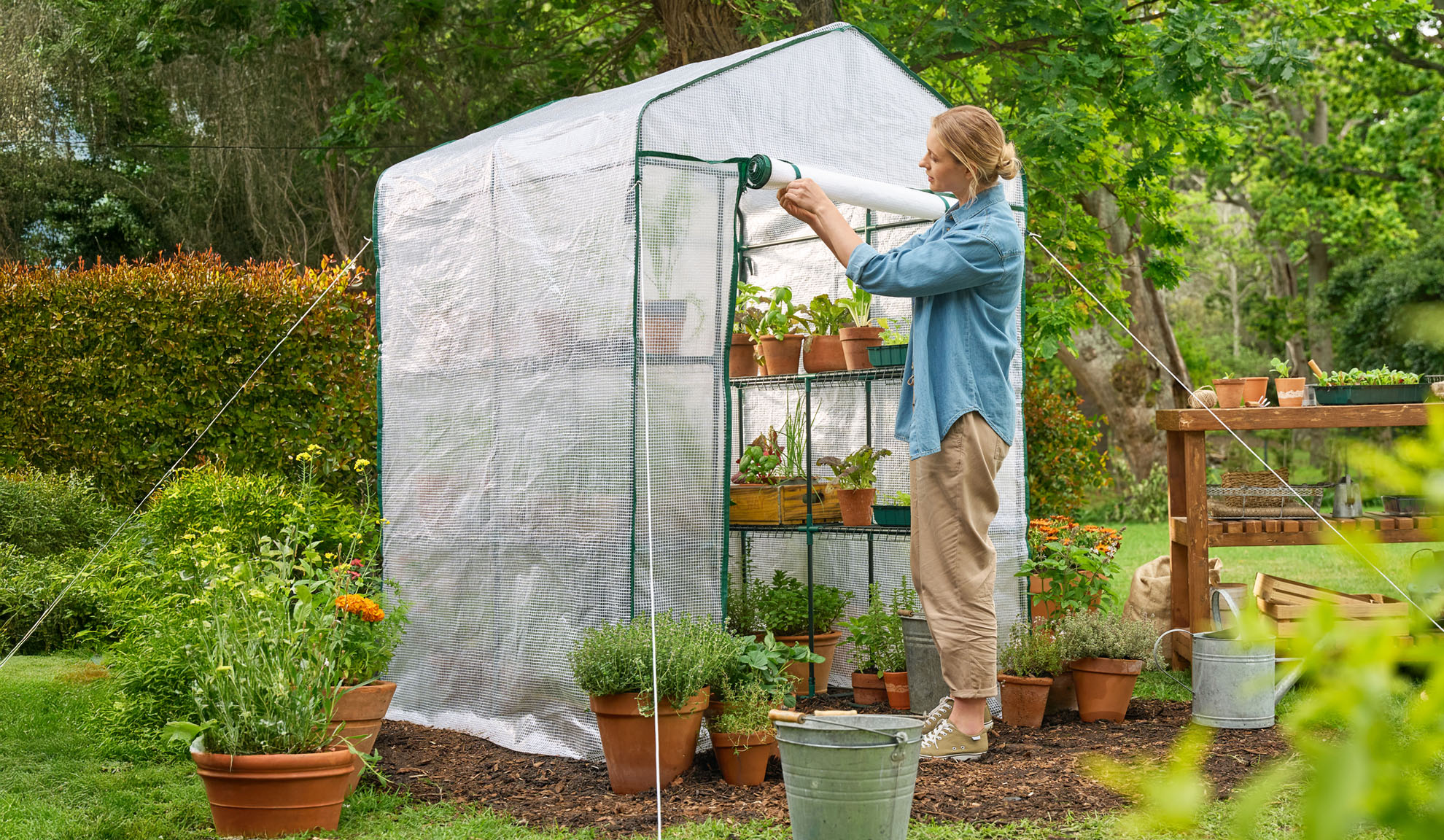 Femme dans le jardin ouvrant une serre avec des plantes et des semis.