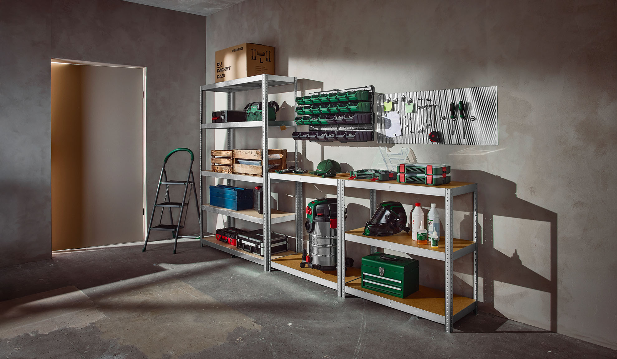 Un garage ou atelier bien organisé avec des étagères métalliques, des bacs de rangement, des outils et un escabeau.