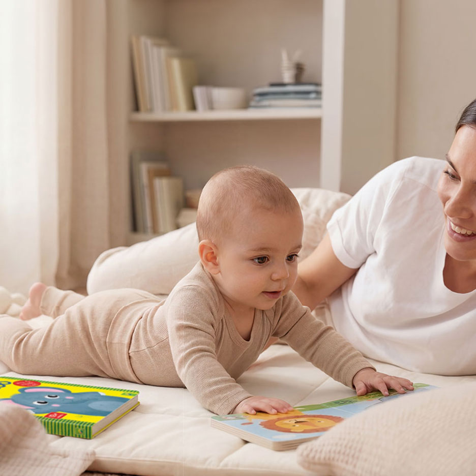 Bébé en body beige jouant avec des livres d'animaux colorés sur un tapis, avec un adulte souriant.