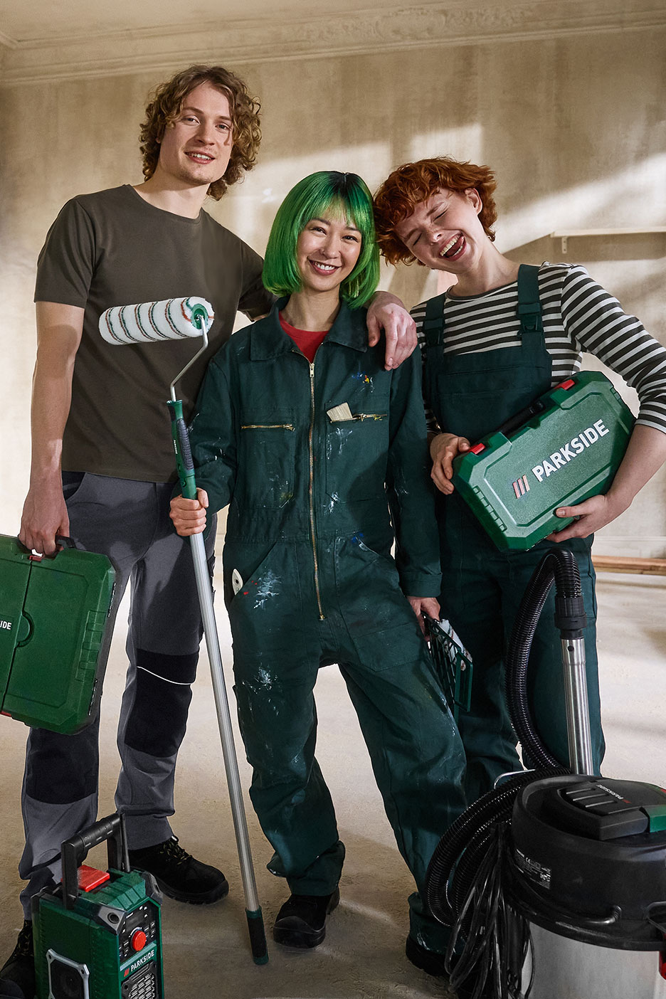 Trois personnes souriantes avec des outils de rénovation, dont un rouleau à peinture et une boîte à outils.