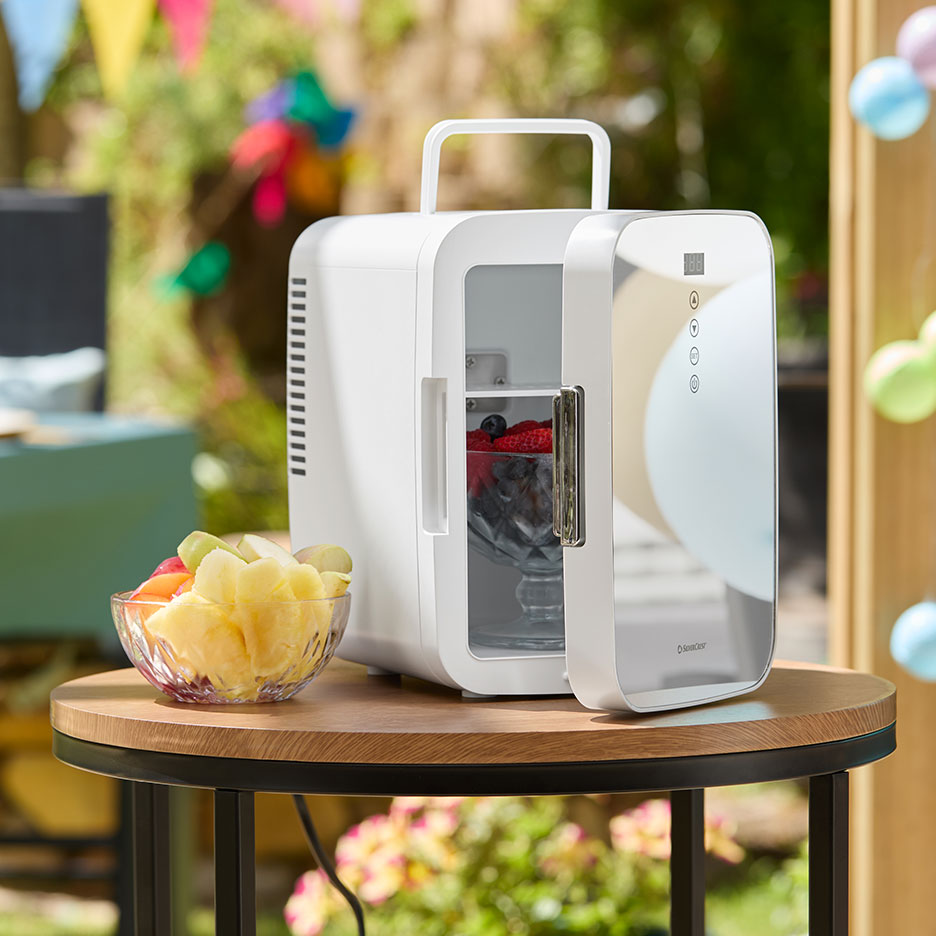 Mini-réfrigérateur portable blanc avec fruits frais sur une table d'extérieur.