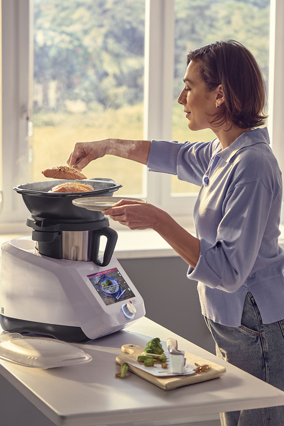 Femme préparant du saumon et des légumes avec un robot de cuisine multifonction.