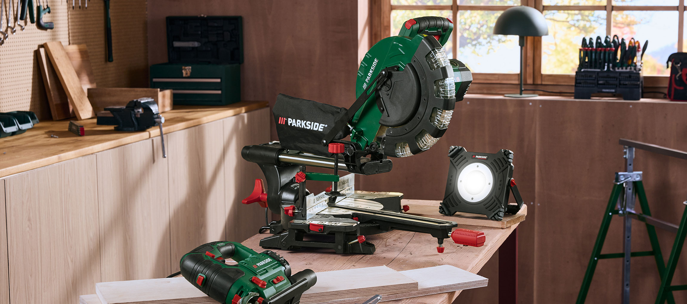 Atelier avec scie à onglet, lampe d'atelier et autres outils sur une table en bois.