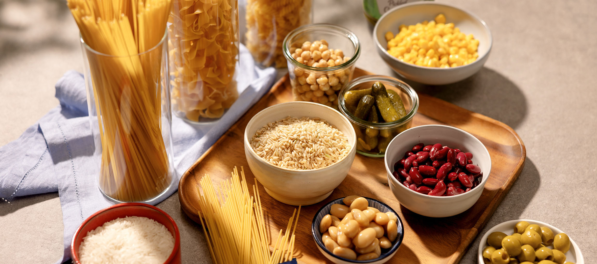 Divers produits de base de garde-manger, y compris pâtes, riz, haricots, pois chiches, maïs, cornichons et olives.