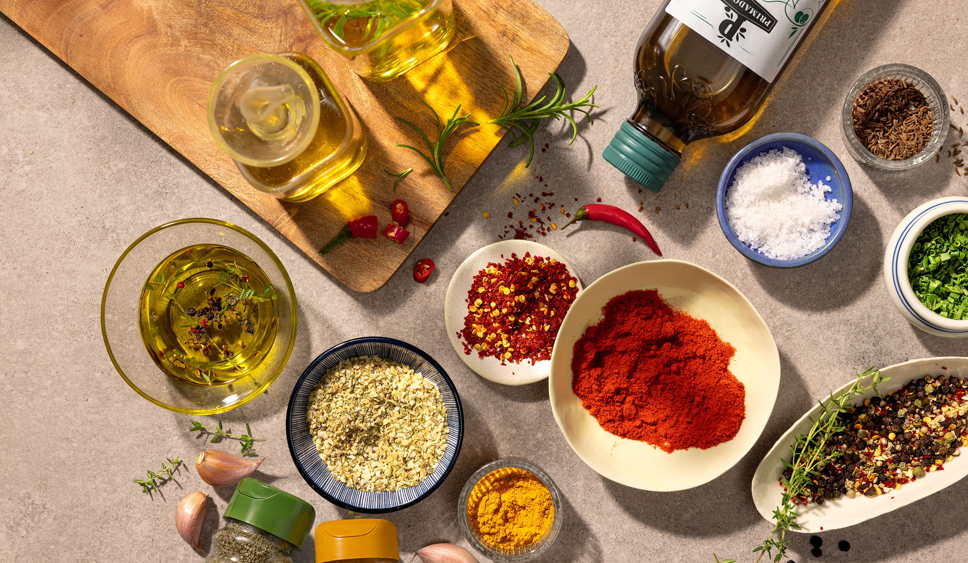 Huile d'olive, épices et piments sur une planche à découper en bois et un comptoir en béton.