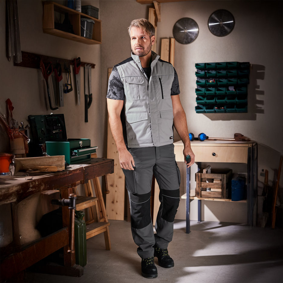 Un homme porte un gilet et un pantalon de travail dans un atelier.