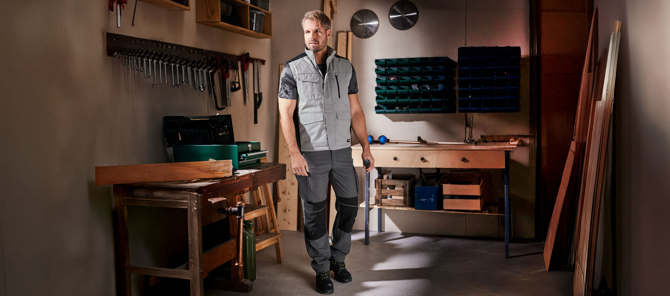 Un homme en vêtements de travail et gilet se trouve dans un atelier.