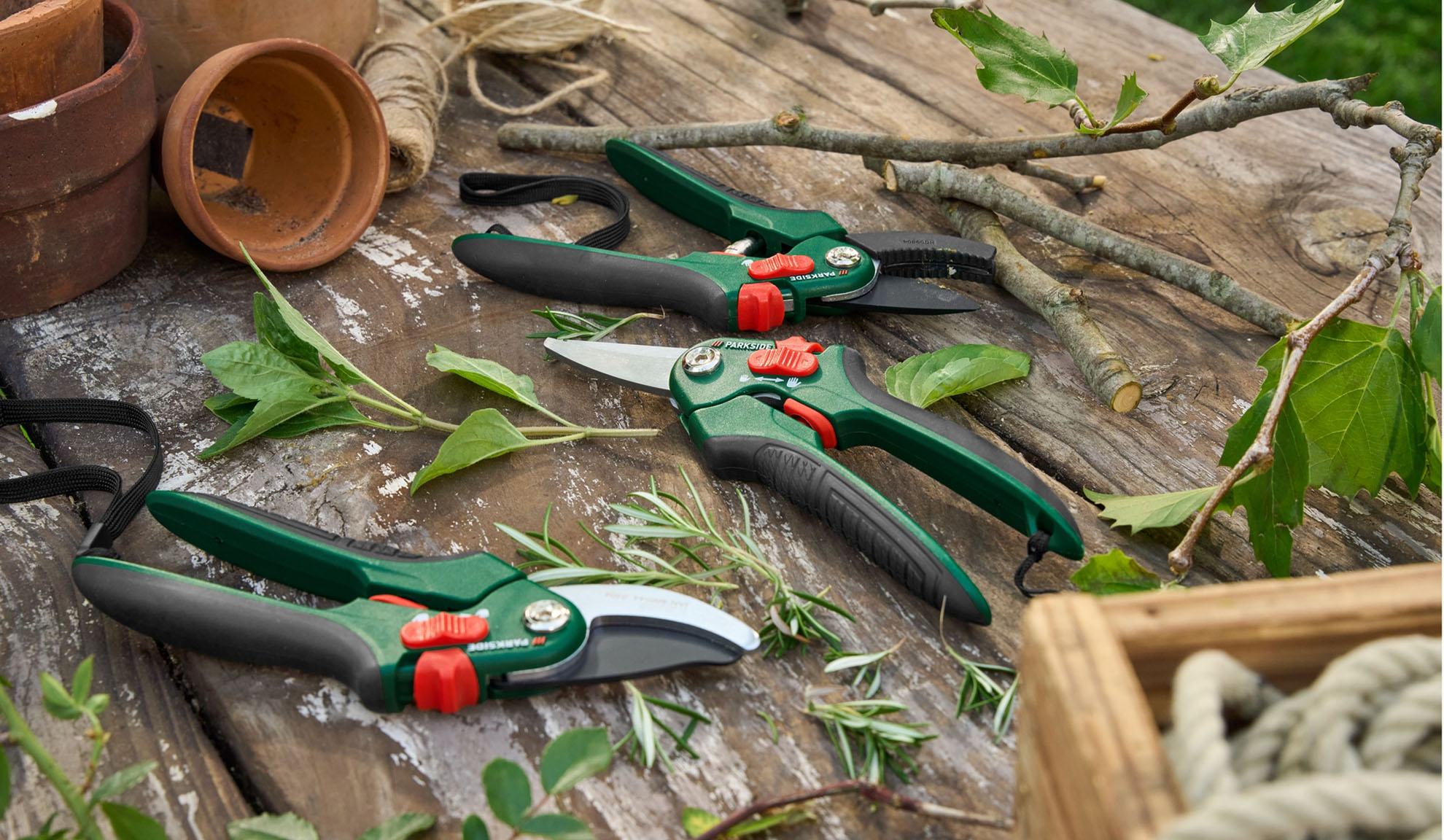 Des ciseaux de jardinage et des sécateurs Parkside reposent sur une surface en bois rustique avec des plantes et des fournitures de jardinage.