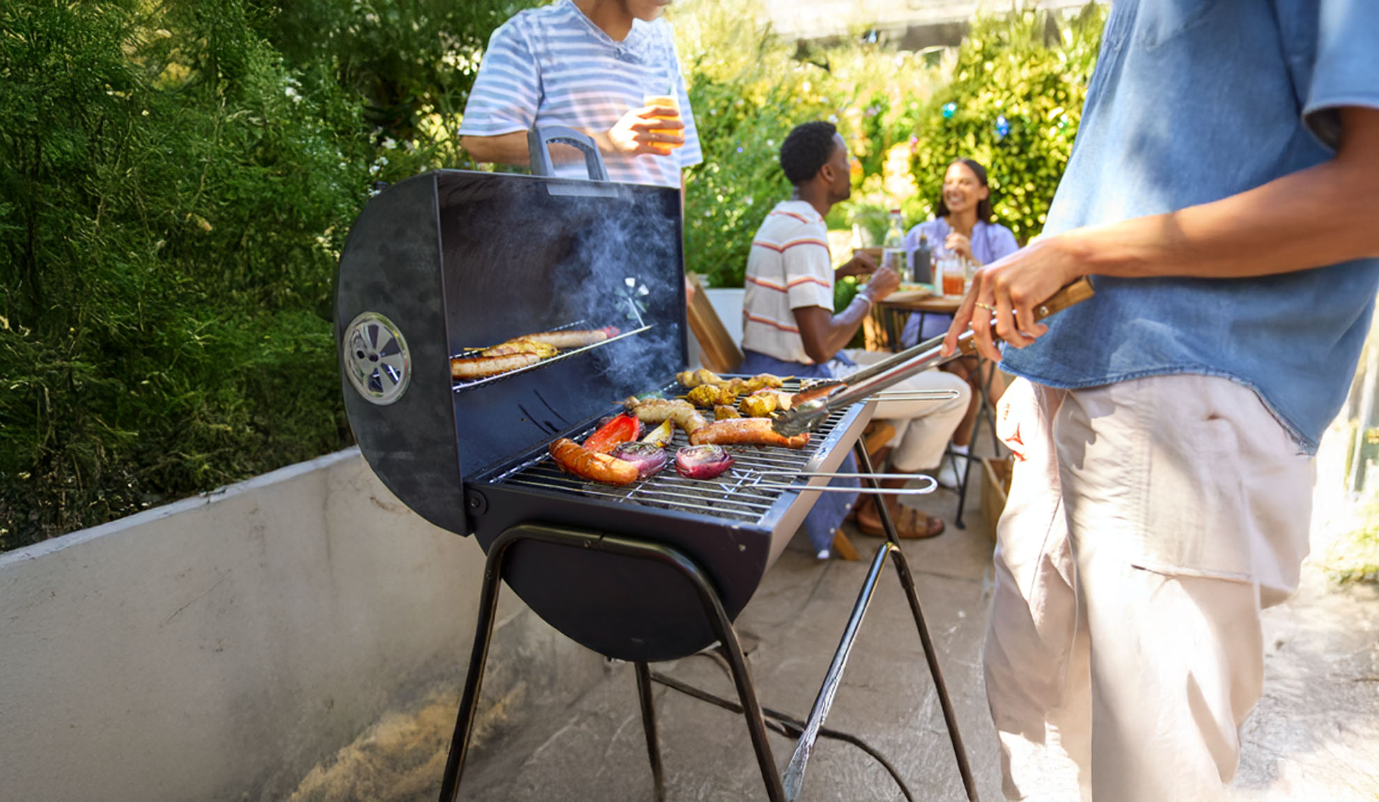 Des amis font un barbecue avec des saucisses et des légumes dans leur jardin.