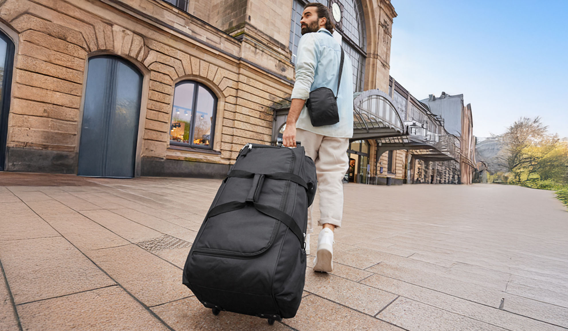 Un homme marche avec une valise à roulettes près d'une gare.