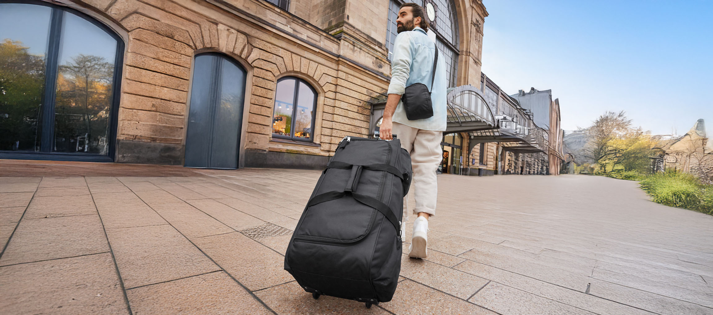 Un homme tire une valise à roulettes loin d'une gare.