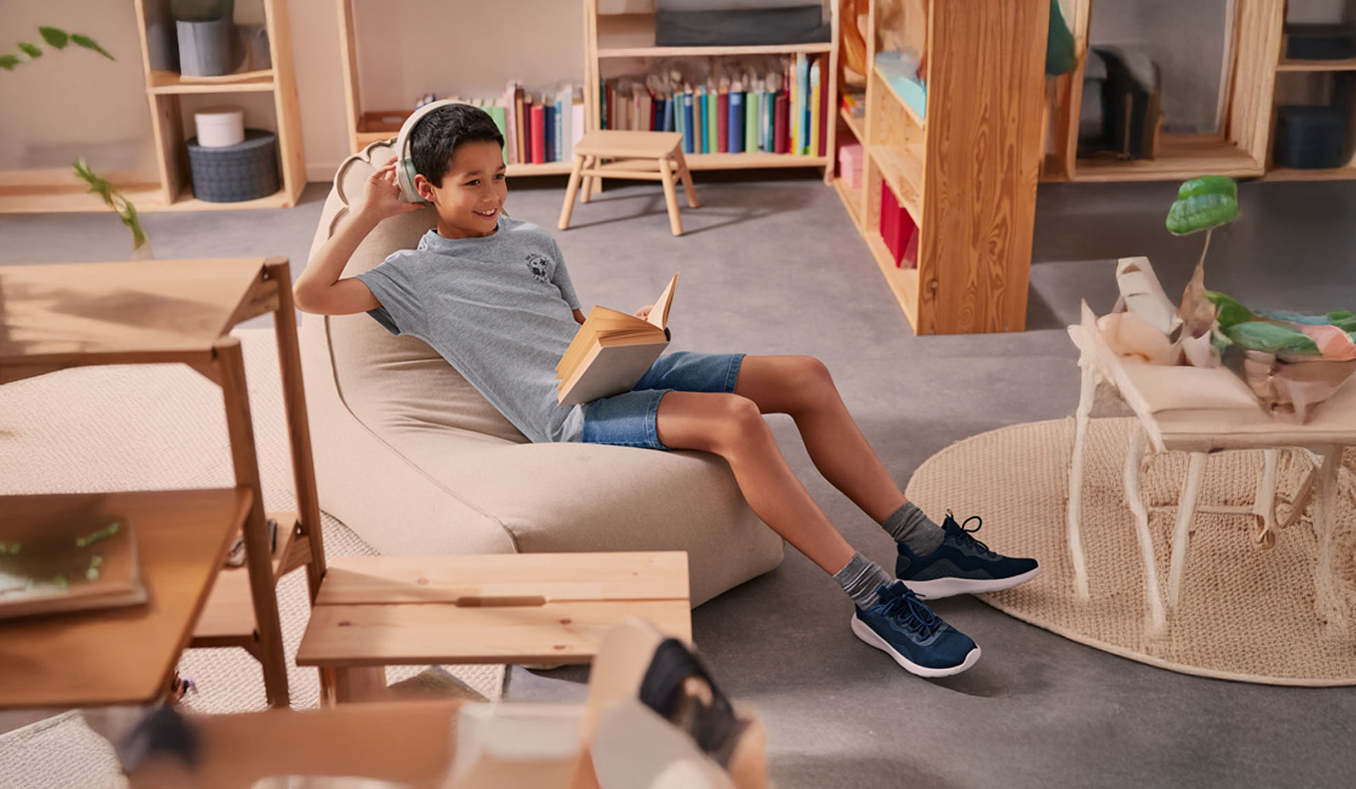 Un garçon se détend dans un pouf, porte des écouteurs et lit un livre.
