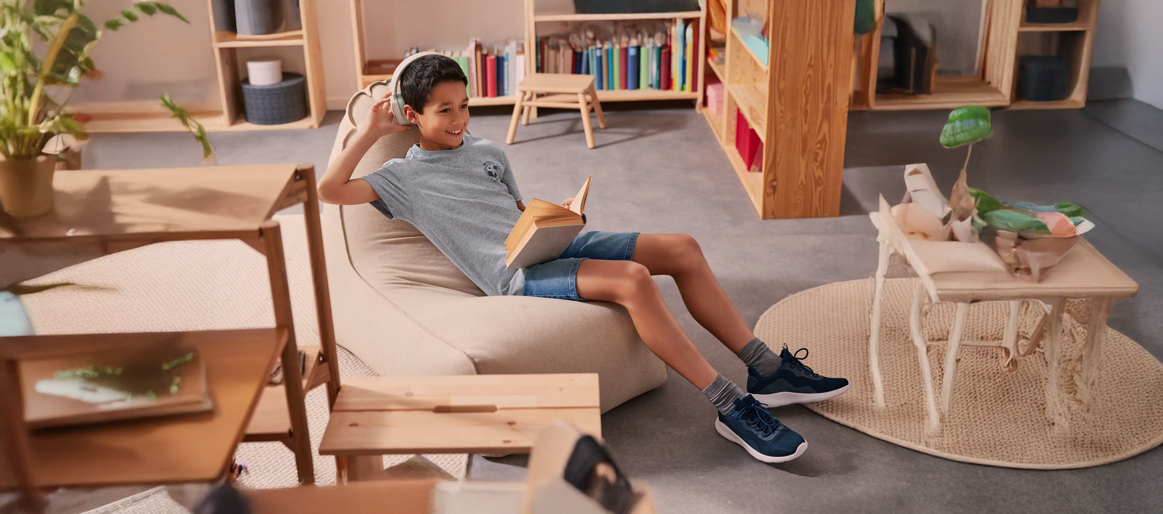 Un garçon se détend dans un pouf, lisant un livre avec des écouteurs.