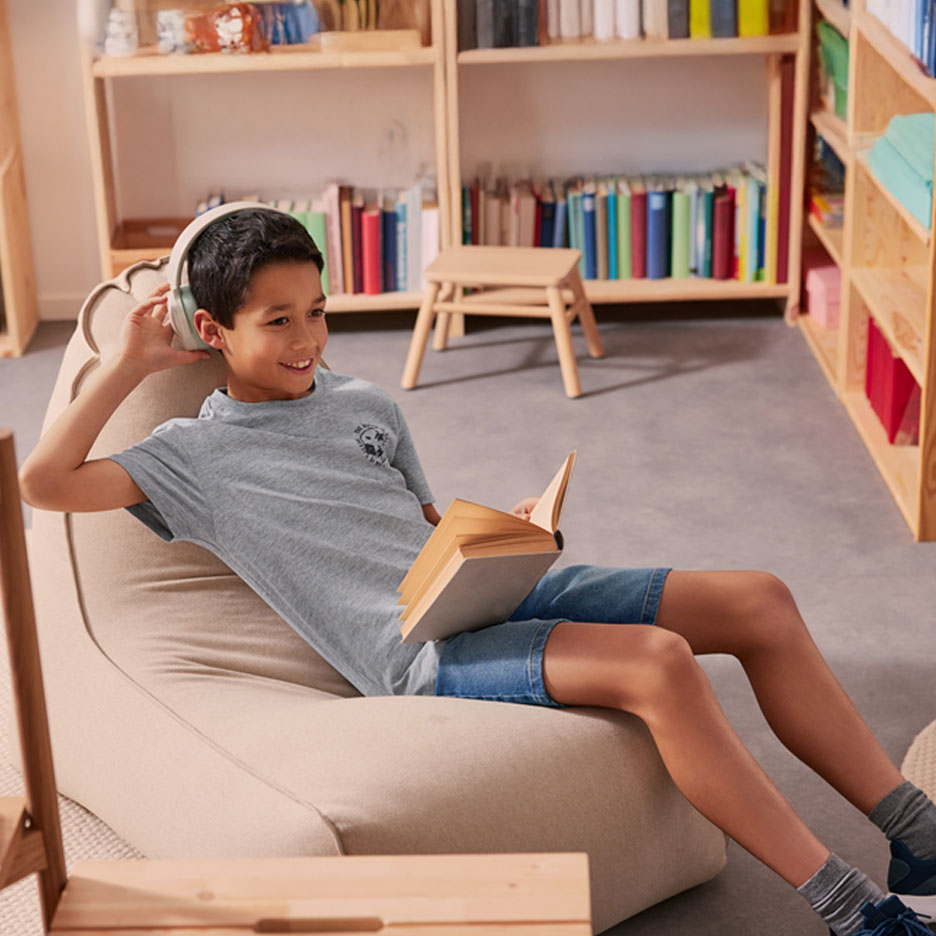 Un garçon avec des écouteurs lit un livre dans un pouf.