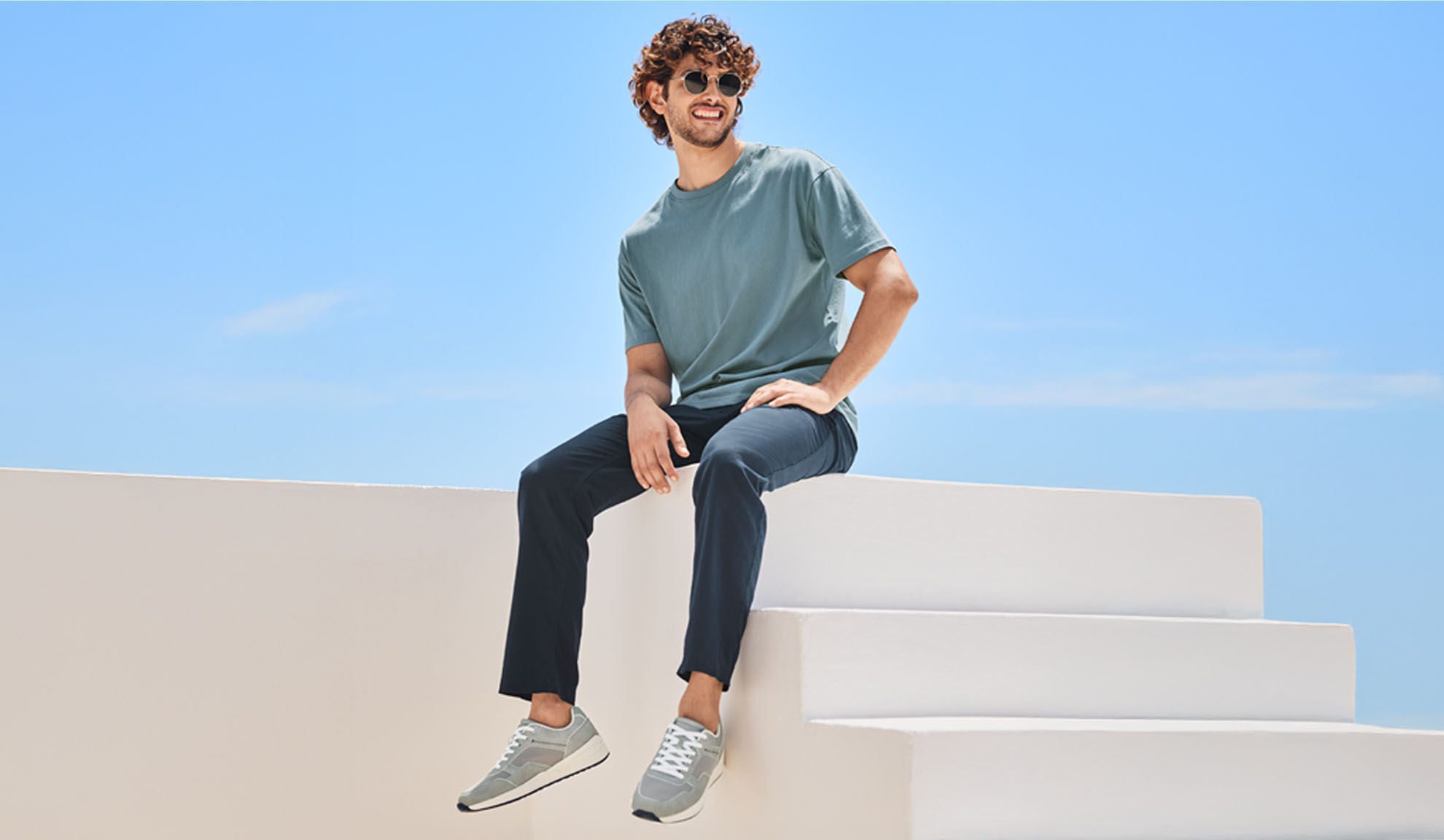 Un homme détendu portant un t-shirt et un pantalon bleu foncé, assis sur un escalier blanc.